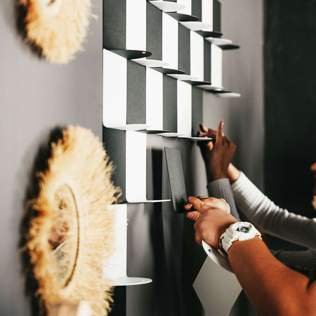 Two people arranging modern wall shelving with black and white colors for stylish home entertainment.