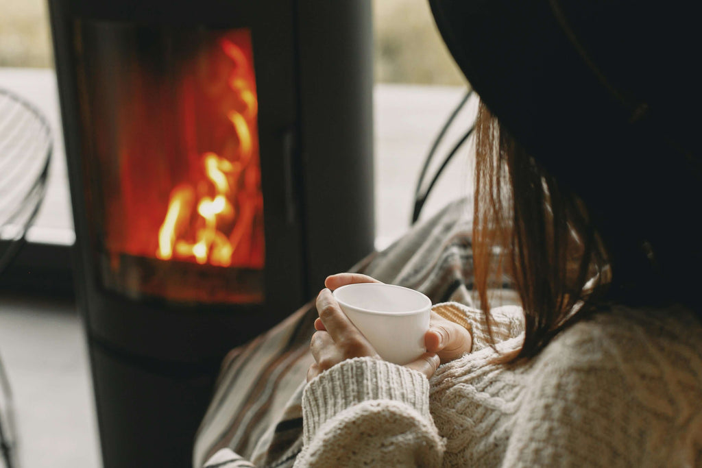 Cozy winter scene of a woman holding a cup by a warm fireplace, exuding comfort and warmth.