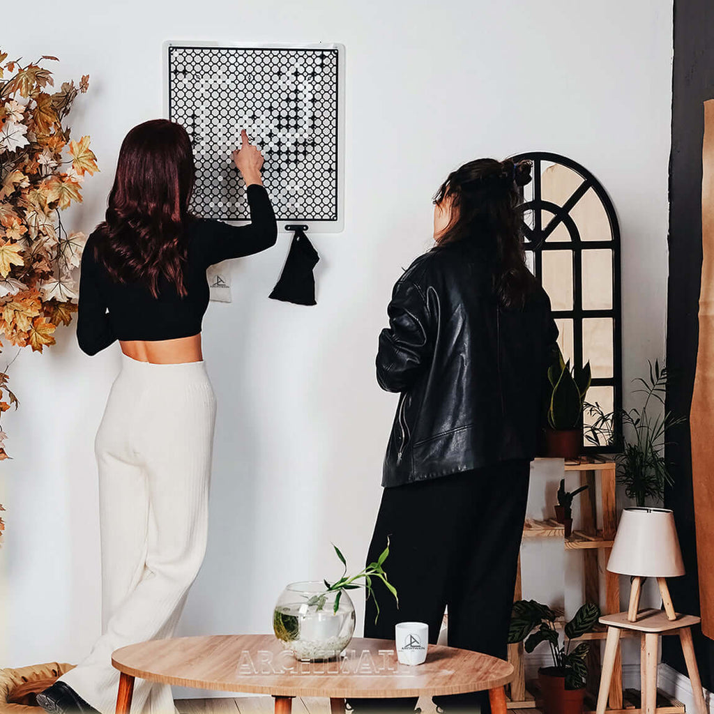 Two women engaged in creative play, interacting with a wall art piece in a cozy, modern interior space.