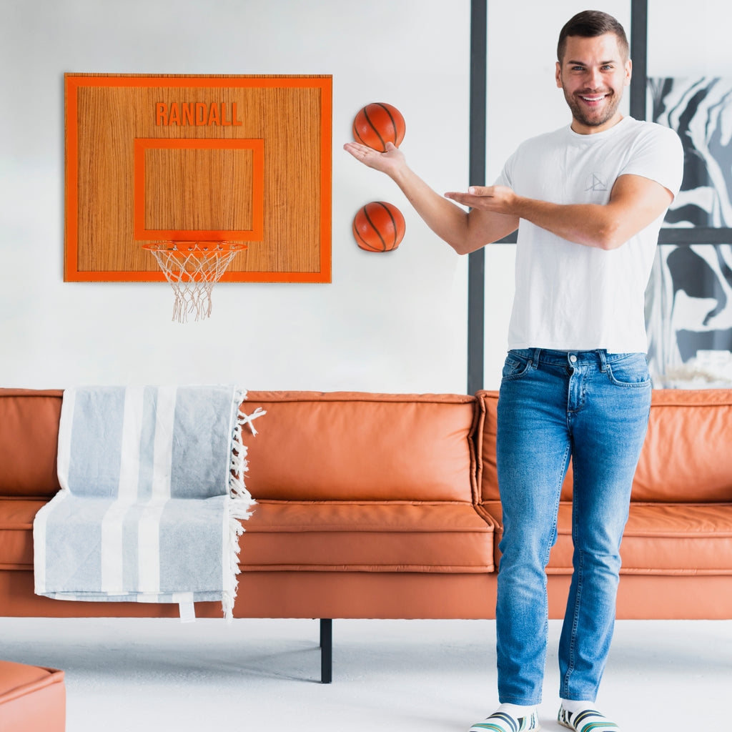 Man showcasing personalized wooden wall hoop with basketballs above a stylish sofa in modern living room.