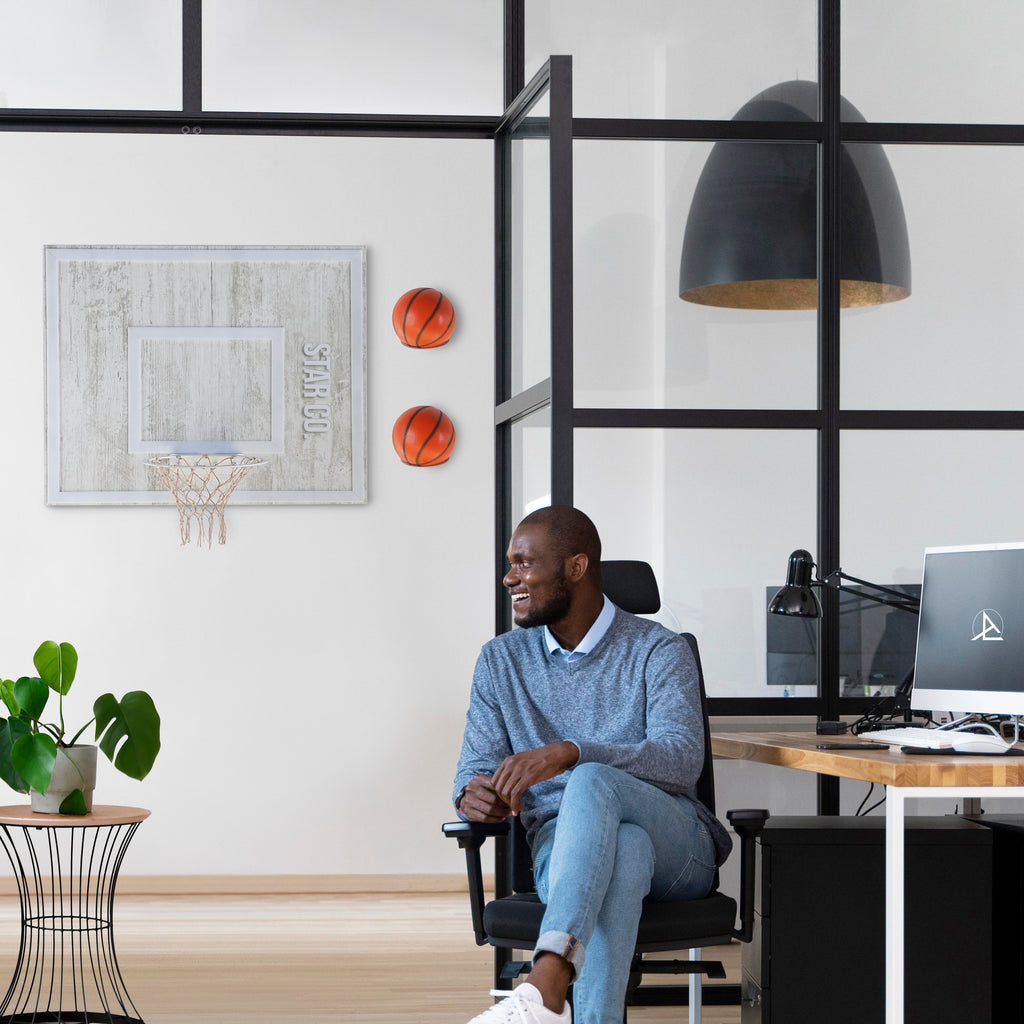 Man enjoying leisure time in a modern office with a wooden wall hoop and basketballs for entertainment.